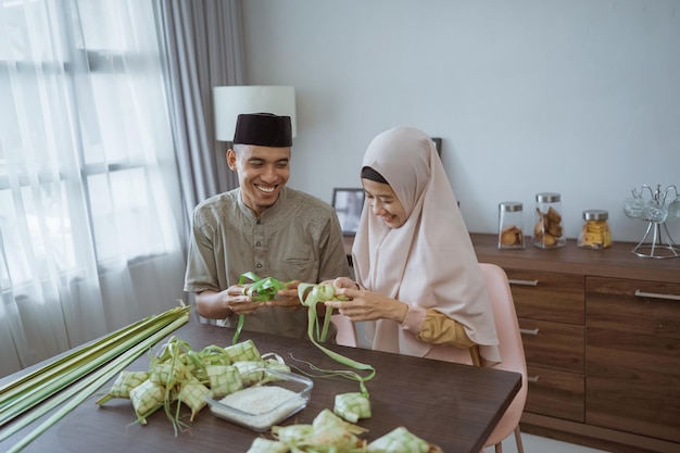 Muslimisches paar asiatisch, das zu hause ketupat-reiskuchen mit palmblatt macht