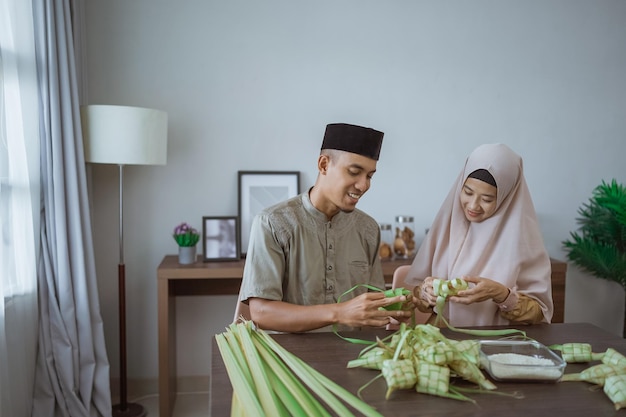 Muslimisches paar asiatisch, das zu hause ketupat-reiskuchen mit palmblatt macht