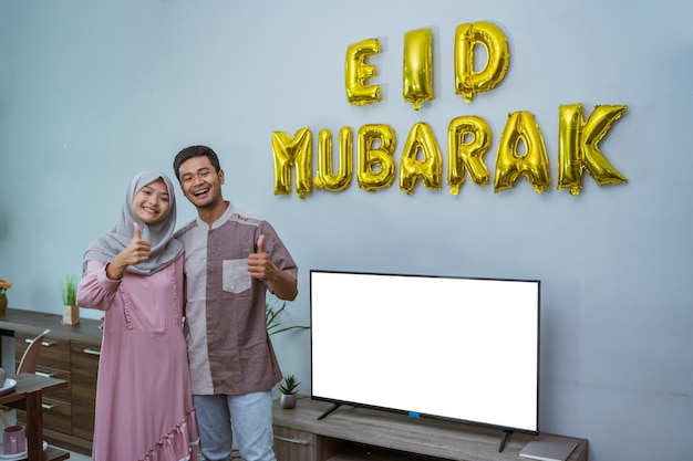 Muslimisches paar, das sein haus mit eid mubarak-text mit dem daumen oben verziert