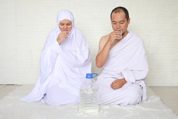 Muslimisches Paar, das weiße Ihram-Kleidung trägt und Zamzam-Wasser trinkt