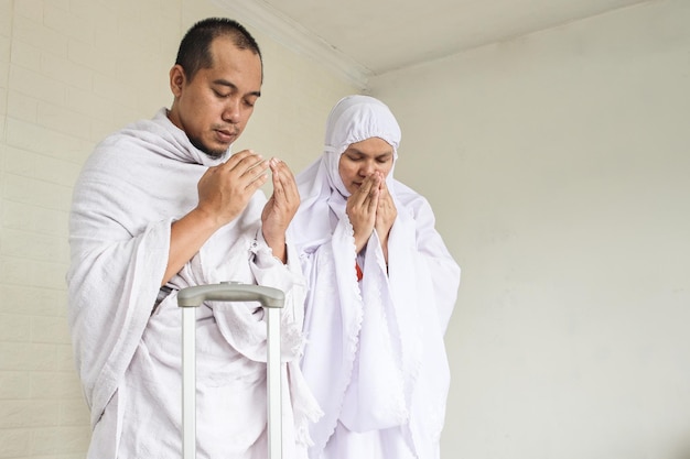 Muslimisches Paar trägt weißes Ihram und betet, bevor es zur Umrah und Hajj geht