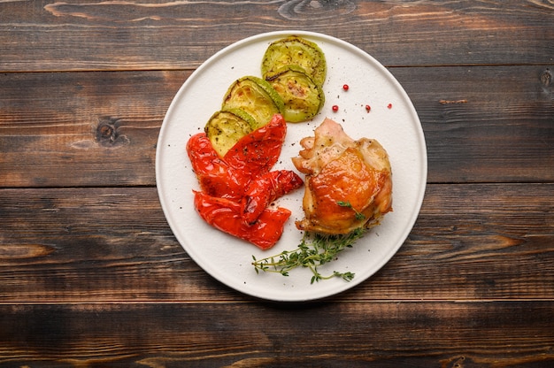 Muslo de pollo al horno casero, calabacín y pimientos con salsa de soja, especias y hierbas en un plato blanco sobre una superficie de madera