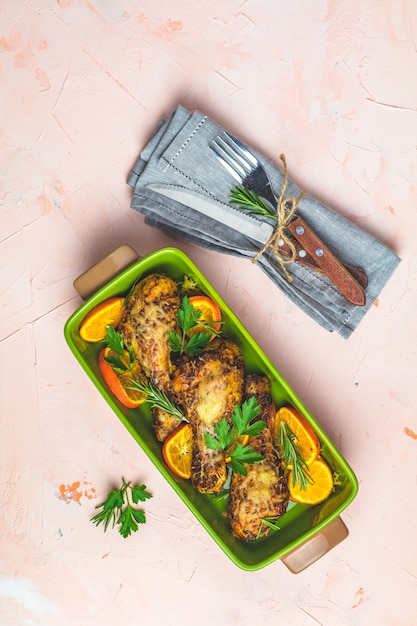 Muslo de pollo al horno en un plato verde con naranja y romero