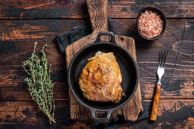 Muslo de pollo al horno en una sartén con romero y sal. Mesa de madera oscura. Vista superior.