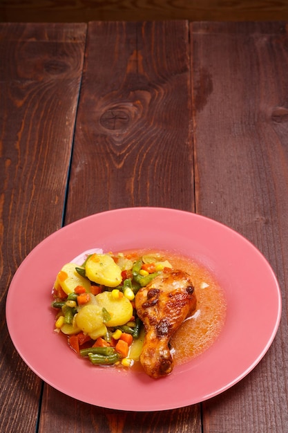 Muslo de pollo al horno con verduras, patatas, judías verdes en salsa y especias en un espacio de mesa de madera