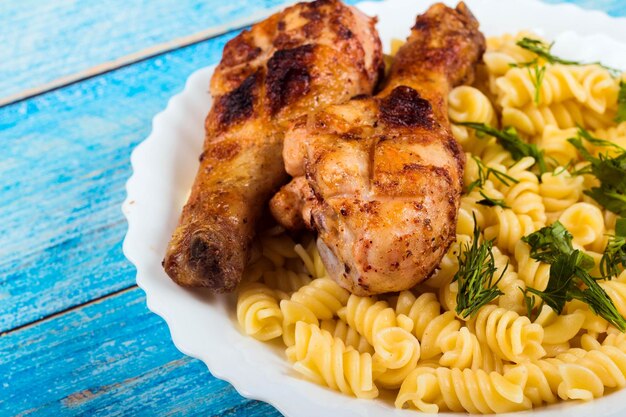 Muslo de pollo a la parrilla y pasta en plato blanco fondo de madera azul