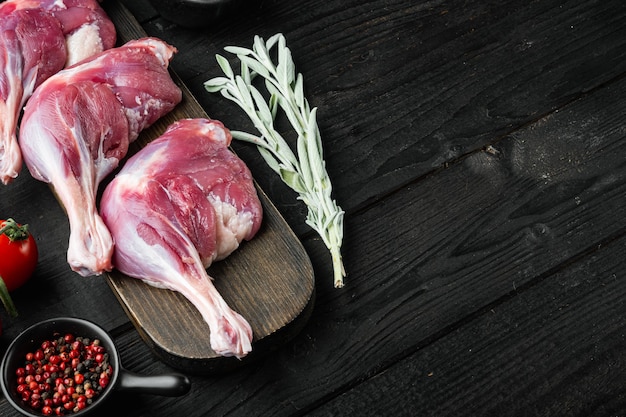 Muslos de pierna de pato crudo, con hierbas e ingredientes, sobre mesa de madera negra