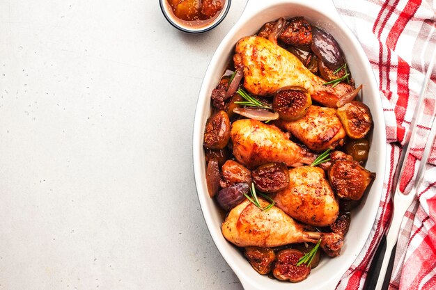 Muslos de pollo al horno con higos y cebollas rojas en adobo balsámico en una fuente de cerámica para hornear fondo blanco vista superior