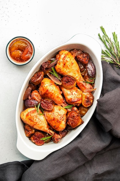 Muslos de pollo al horno con higos y cebollas rojas en adobo balsámico en una fuente de cerámica para hornear fondo blanco vista superior