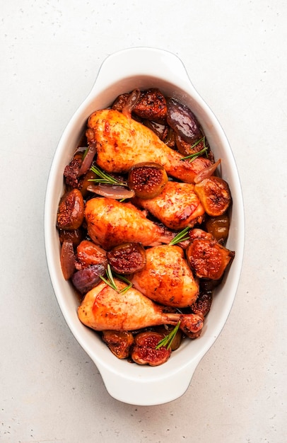 Muslos de pollo al horno con higos y cebollas rojas en una fuente de horno de cerámica vista superior de fondo de mesa de cocina blanca