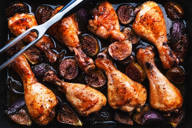 Muslos de pollo al horno con higos dulces y cebollas en adobo balsámico sobre una bandeja para hornear negra vista superior de fondo de mesa verde oxidado