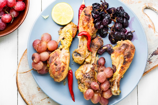 Muslos de pollo al horno con uvas sobre fondo blanco.