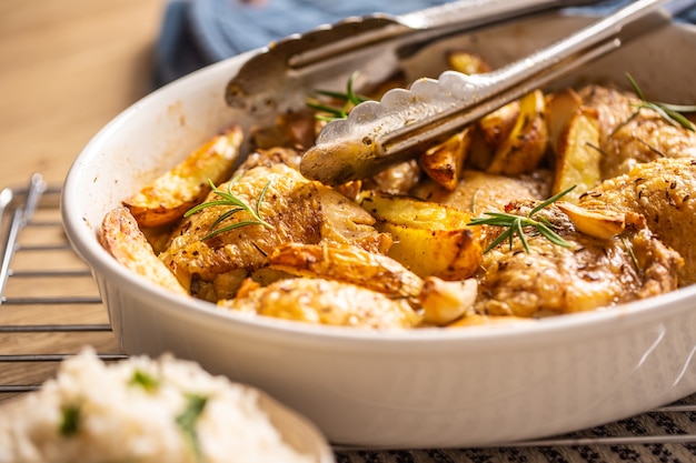 Muslos de pollo asados con patatas americanas en una fuente para hornear.