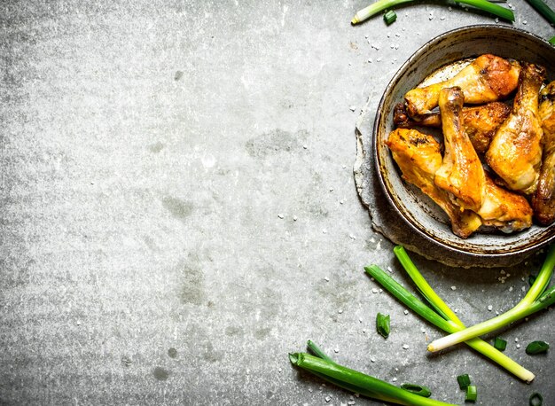 Muslos de pollo con cebollas verdes. Sobre un fondo de piedra.