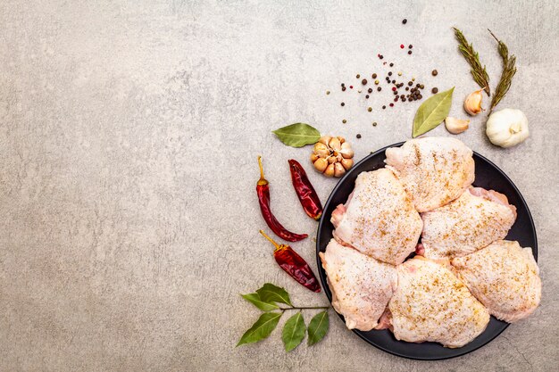 Muslos de pollo crudo con especias. Ingredientes para cocinar carne sobre una superficie de piedra. Pimienta picante y negra, ajo, romero, laurel, copia espacio.