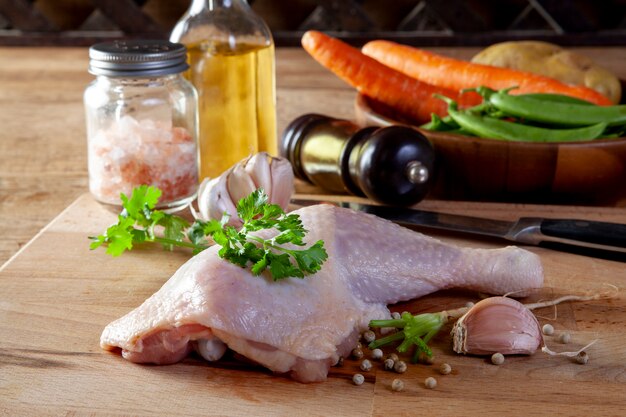 Muslos de pollo crudo con especias y verduras en una tabla de madera