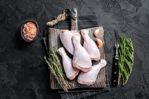 Muslos de pollo crudo fresco piernas sobre tabla de cortar de madera. Fondo negro. Vista superior.