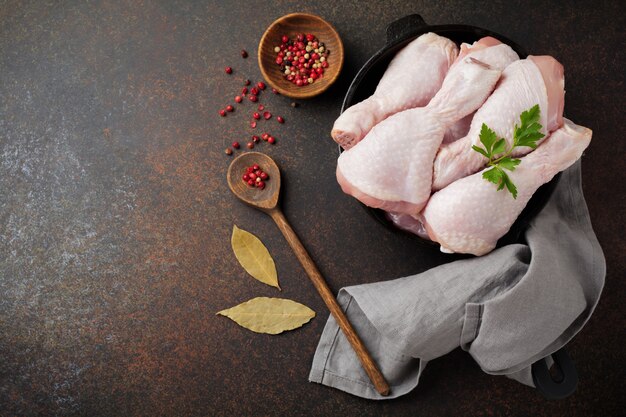 Muslos de pollo crudo en una olla de hierro fundido con especias y hierbas sobre un hormigón oscuro o piedra preparada para cocinar.