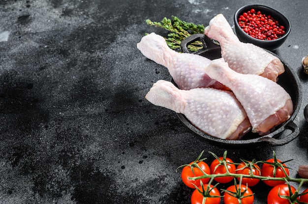 Muslos de pollo crudo, patas con hierbas y especias en una sartén. Carne de aves de corral ecológica. Fondo negro. Vista superior. Copia espacio