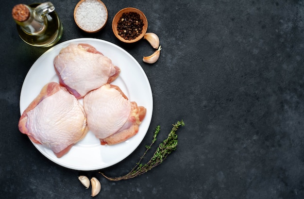 Muslos de pollo crudo en un plato blanco con especias sobre un fondo de piedra