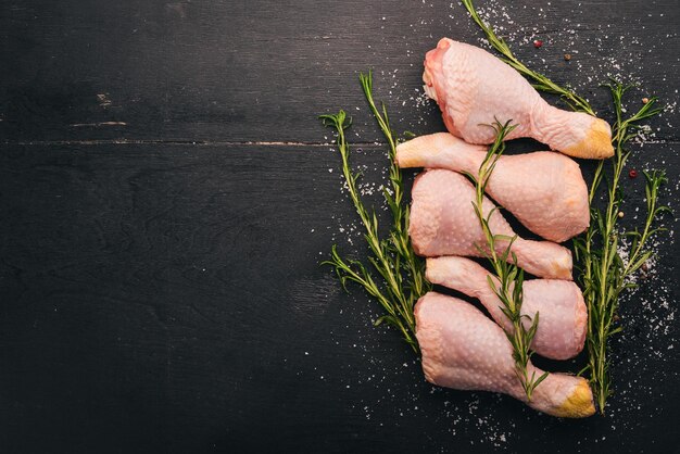 Muslos de pollo crudo con romero y especias sobre un fondo de madera negra Vista superior Espacio libre para texto