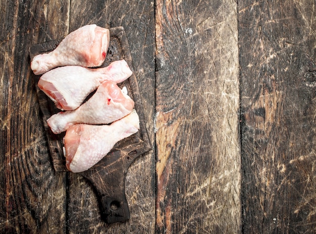 Muslos de pollo crudo en tabla de cortar sobre mesa de madera.