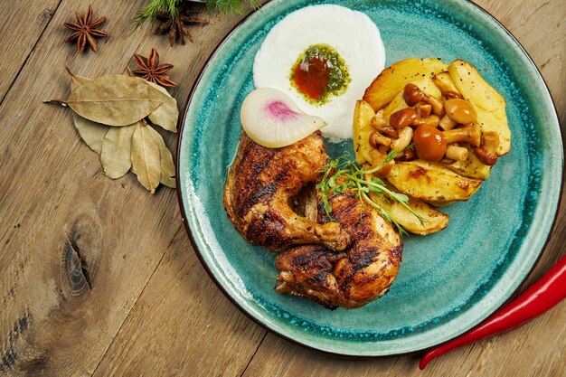 Muslos de pollo a la parrilla con papas al horno y salsa de yogur turco en un plato azul sobre una superficie de madera. Sabrosa comida turca