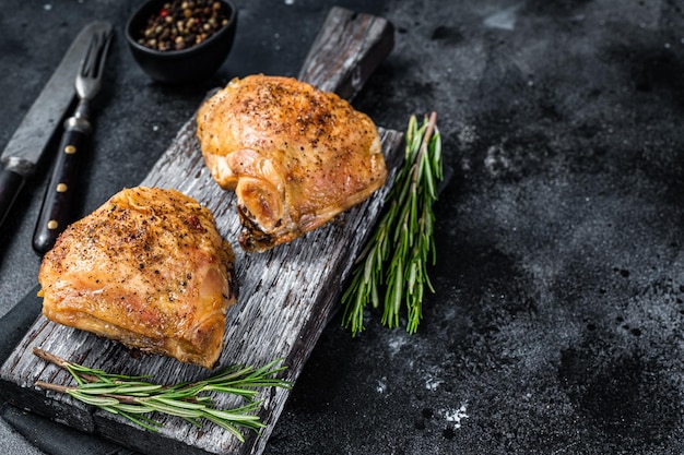 Muslos de pollo a la parrilla picante barbacoa sobre una tabla de madera con romero. Fondo negro. Vista superior. Copie el espacio.