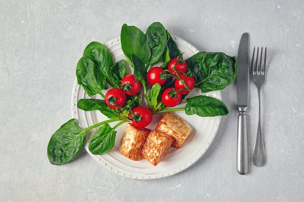 Mussarela halloumi de requeijão frito com espinafre verde e tomate cereja em um galho sobre uma mesa de concreto cinza