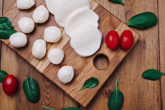 Mussarela pequena branca, bolinhos de queijo, folhas de espinafre e tomates em uma placa de madeira