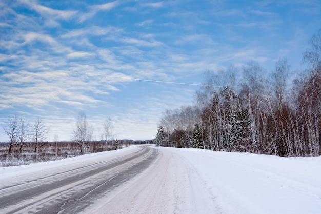 Muster auf der Winterautobahn in Form von vier geraden Linien. Verschneite Straße auf dem Hintergrund des schneebedeckten Waldes. Winterlandschaft.