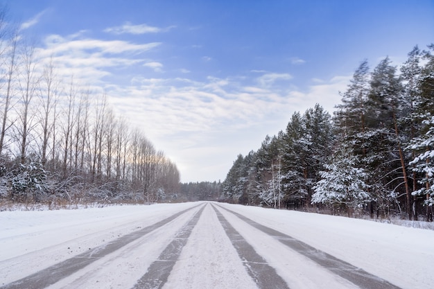 Muster auf der Winterautobahn in Form von vier geraden Linien. Verschneite Straße auf dem Hintergrund des schneebedeckten Waldes. Winterlandschaft.
