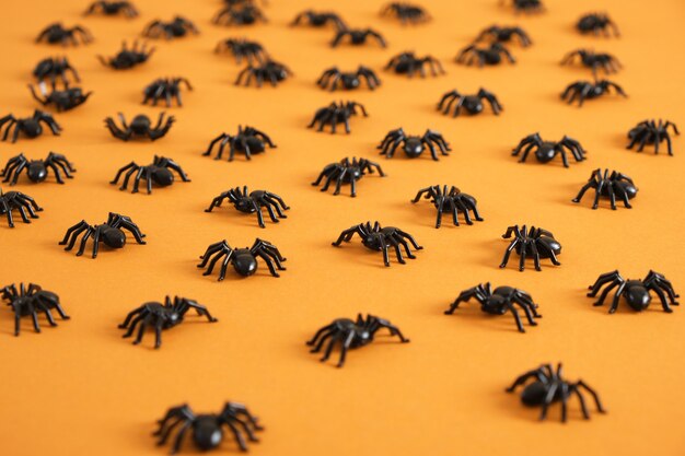 Muster aus schwarzen Plastikspinnen auf orangem Hintergrund. Halloween. Trick-or-Treat-Konzept. Ansicht von oben. Fröhliches Halloween