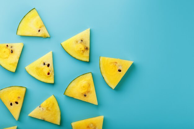 Muster von Scheiben der frischen gelben Wassermelone auf einem Blau. Von oben betrachten. Freiraum