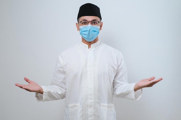 Musulmán asiático sonriendo feliz usando máscara facial para saludar durante la celebración del Ramadán con ambos brazos abiertos sobre fondo blanco