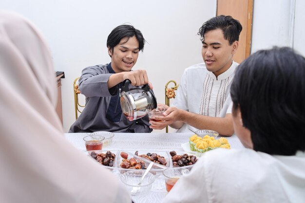 Musulmanes asiáticos vertiendo agua, cenando juntos en casa. Romper el concepto de ayuno.