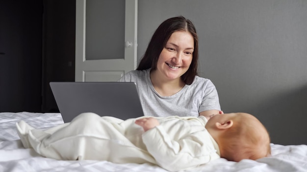 Mutter achtet auf Babymädchen, während sie am Laptop arbeitet