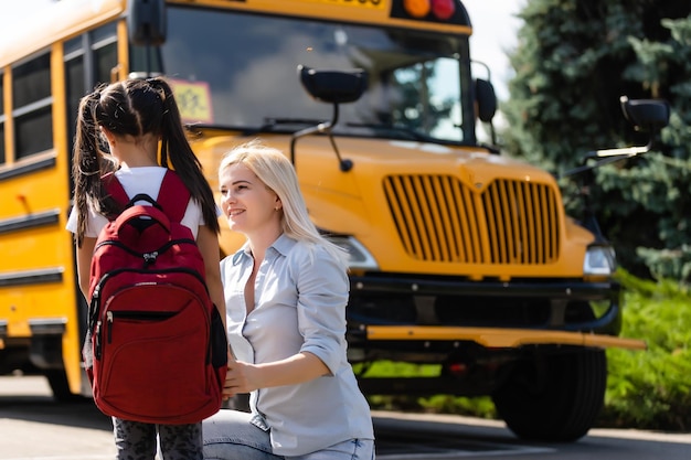 Mutter begleitet das Schulmädchen mit Pferdeschwanz und Rucksack zur Schule.