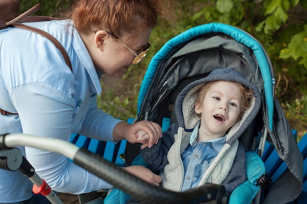 Mutter beugt sich zu ihrem behinderten Sohn im Rollstuhl in einem Stadtpark