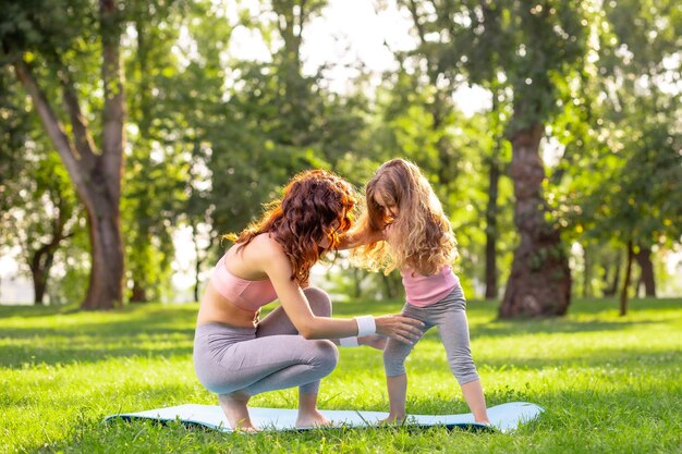 Mutter bringt ihrer kleinen Tochter tagsüber Yoga im Park bei