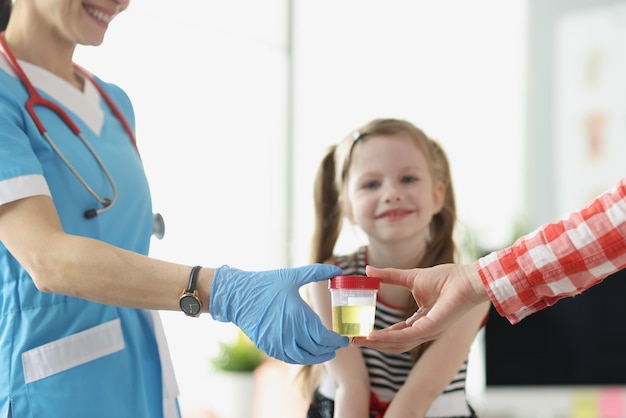 Mutter, die dem Arzt ein Glas Urin vor dem Kind in der Klinik in der Nähe gibt