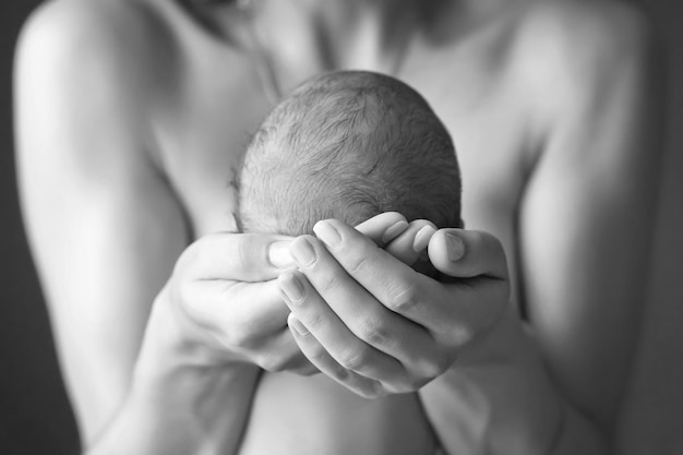 Mutter, die den Kopf ihres neugeborenen Sohnes in den Händen hält Das Baby auf den Händen bei der Mutter Liebevolle Mutterhand, die nettes schlafendes neugeborenes Kind hält