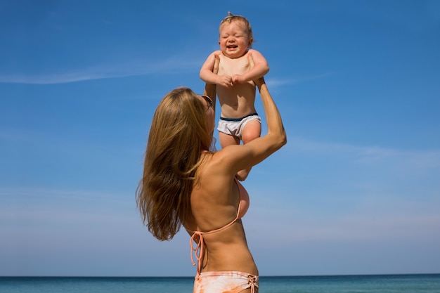 Mutter, die glückliches kleines Baby am Strand hält