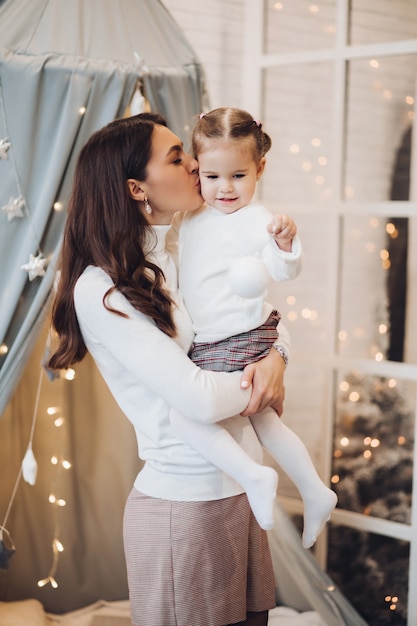 Mutter, die ihre Tochter in der Backe küsst. Zimmer dekoriert für Weihnachten.