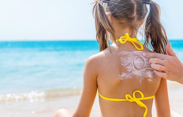 Mutter, die ihrer Tochter am Strand Sonnencreme auf den Rücken schmiert