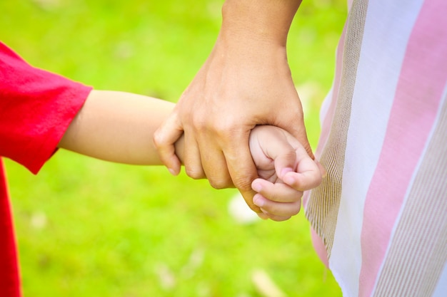 Mutter, die Kinderhand auf grünem Grashintergrund hält.