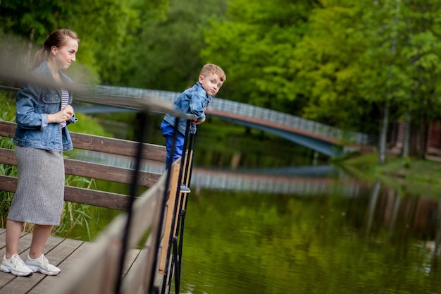 Mutter erlebt, dass das Kind ins Wasser fallen wird Ein kleiner Junge klettert im Park auf ein Brückengeländer Die Gefahr des Ertrinkens Gefahr für Kinder