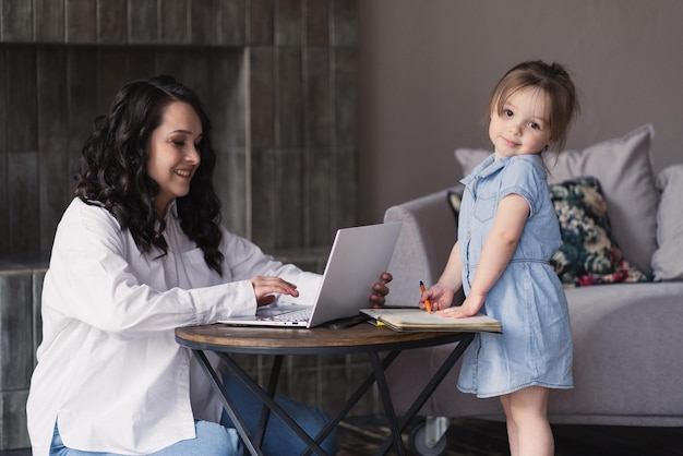 Mutter-Freiberuflerin, die zu Hause mit ihrer Tochter am Laptop arbeitet