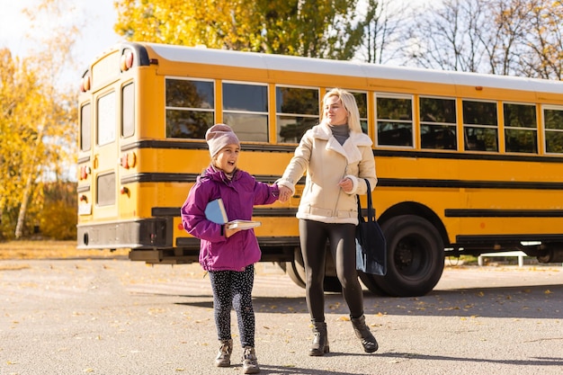 Mutter führt ihre Tochter zum Schulbus vor der Grundschule.