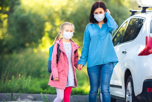 Mutter führt Tochter in Masken zur Schule